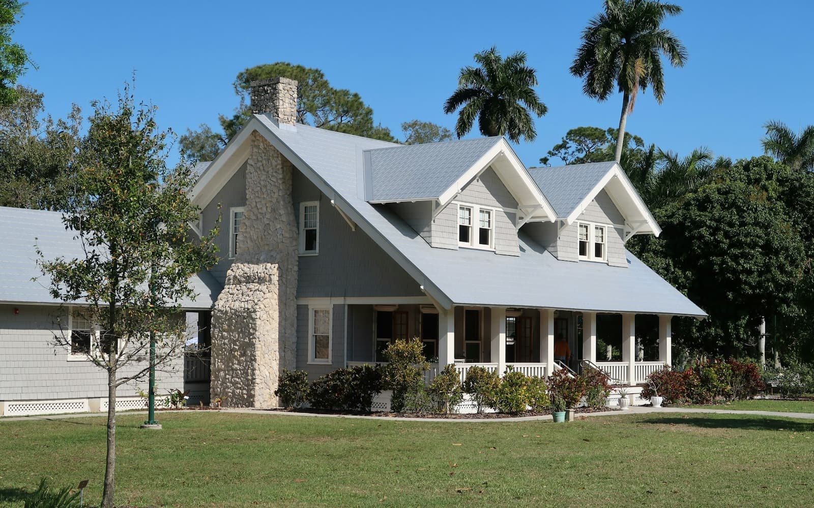A gray house with a metal roof and a stone chimney, with palms behind it