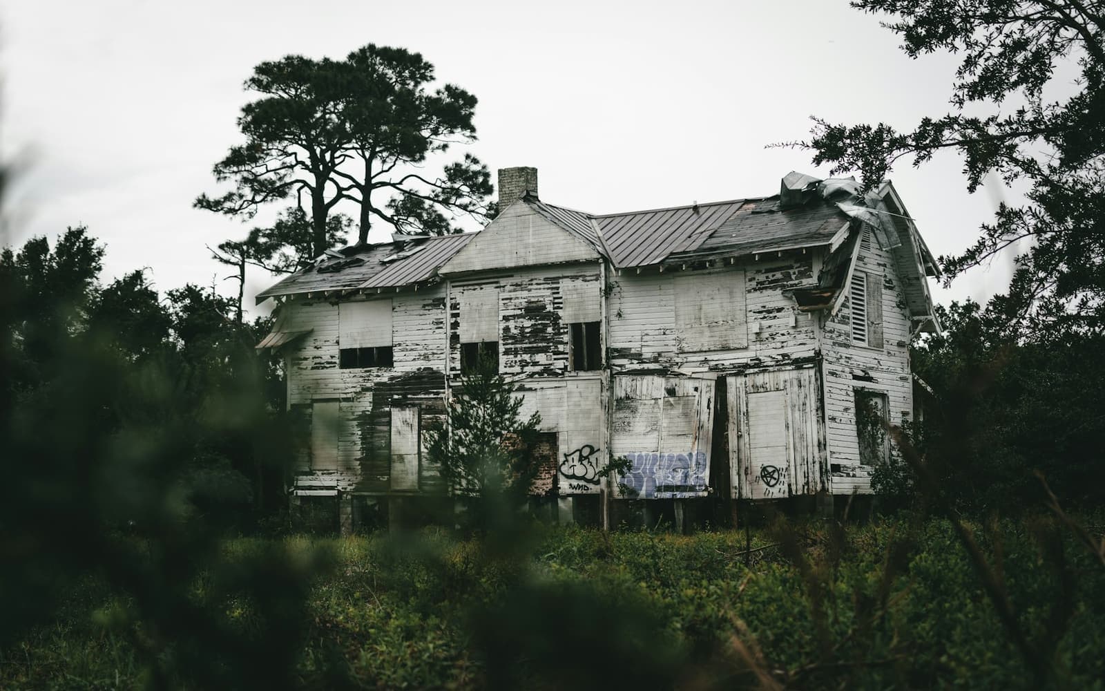 A weathered two-story wooden house behind trees