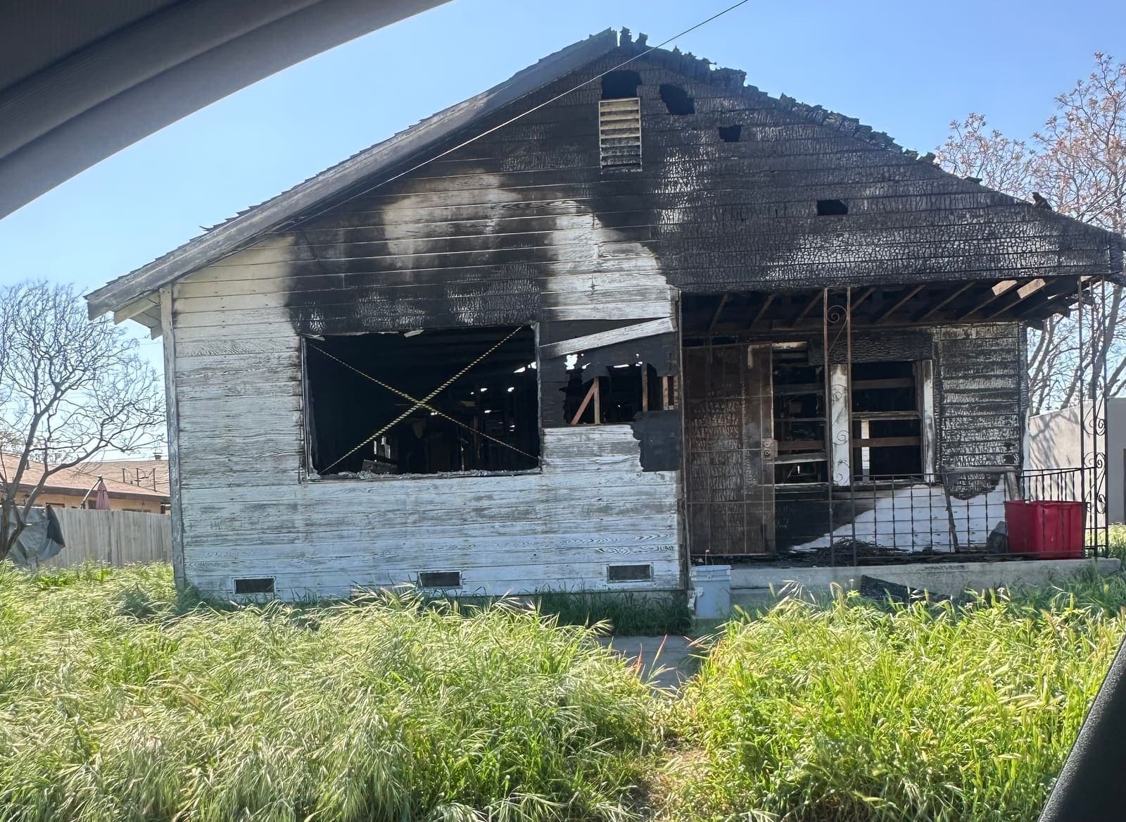 A wood house with heavy fire damage and an overgrown yard