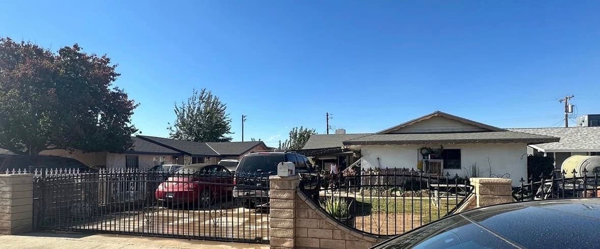 A ranch house behind an iron gate with cars in the driveway